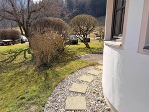 Un sendero conduce a un edificio con borde de piedra, rodeado de césped y árboles.