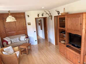 Ein Wohnzimmer mit einer Couch, einem Korbsessel, Holzschränken und aufgehängten Geweihen an der Wand.