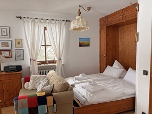 Ein Schlafzimmer mit einem hölzernen Bett, einem Holzschrank, einem Fenster mit Vorhängen und einer Heizung.