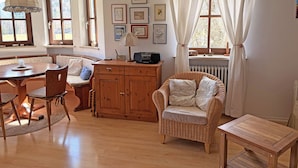 Une pièce chaleureuse avec une table à manger en bois, une chaise en osier, un buffet et une fenêtre avec des rideaux.