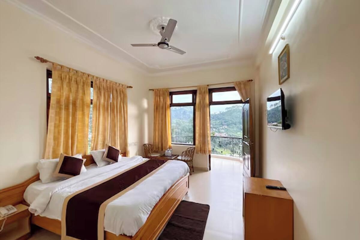 A hotel room with a bed, a desk, a chair, a TV, and a balcony with a view.