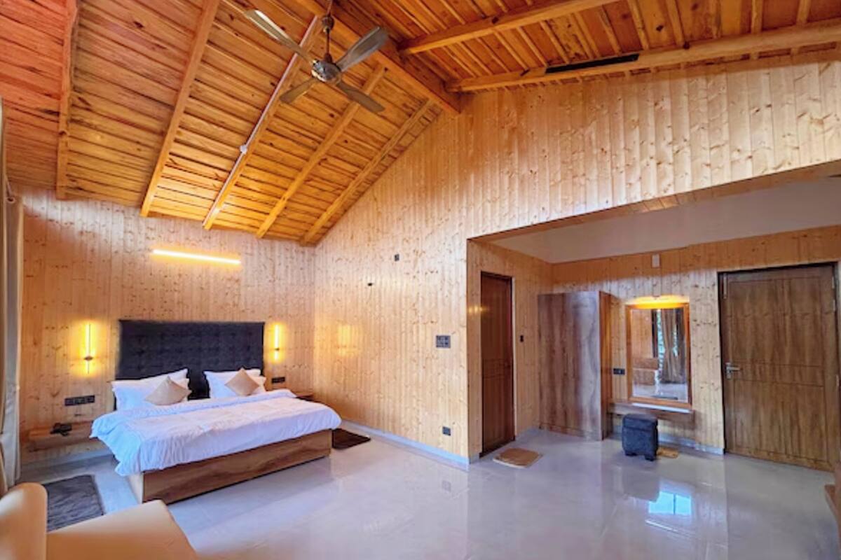 A bedroom with a wooden ceiling, a large bed, a nightstand, and a wall-mounted light.