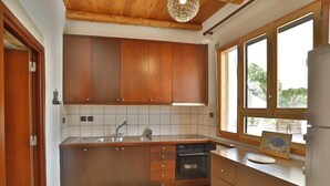 A kitchen with wooden cabinets, a sink, a dishwasher, and a window with a view. - Tholos by Praxithea Stone House & Pool (Chania)