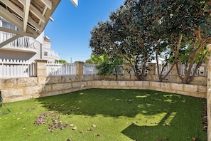 A courtyard with a stone wall, a white fence, and a tree.