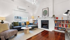A living room with a sofa, a coffee table, a fireplace, a bookshelf, and a chandelier. - Heritage Hideaway - North Perth (North Perth)