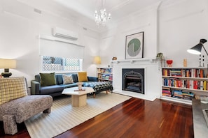 A living room with a sofa, a coffee table, a fireplace, a bookshelf, and a chandelier.