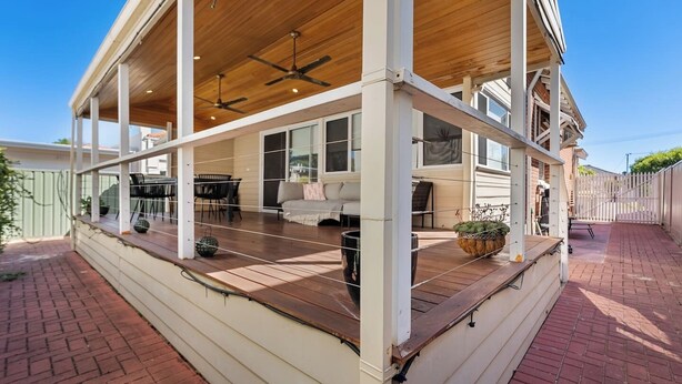 A covered patio with a wooden deck, a seating area with a sofa and chairs, and a view of the adjacent building. - Heritage Hideaway - North Perth (North Perth)