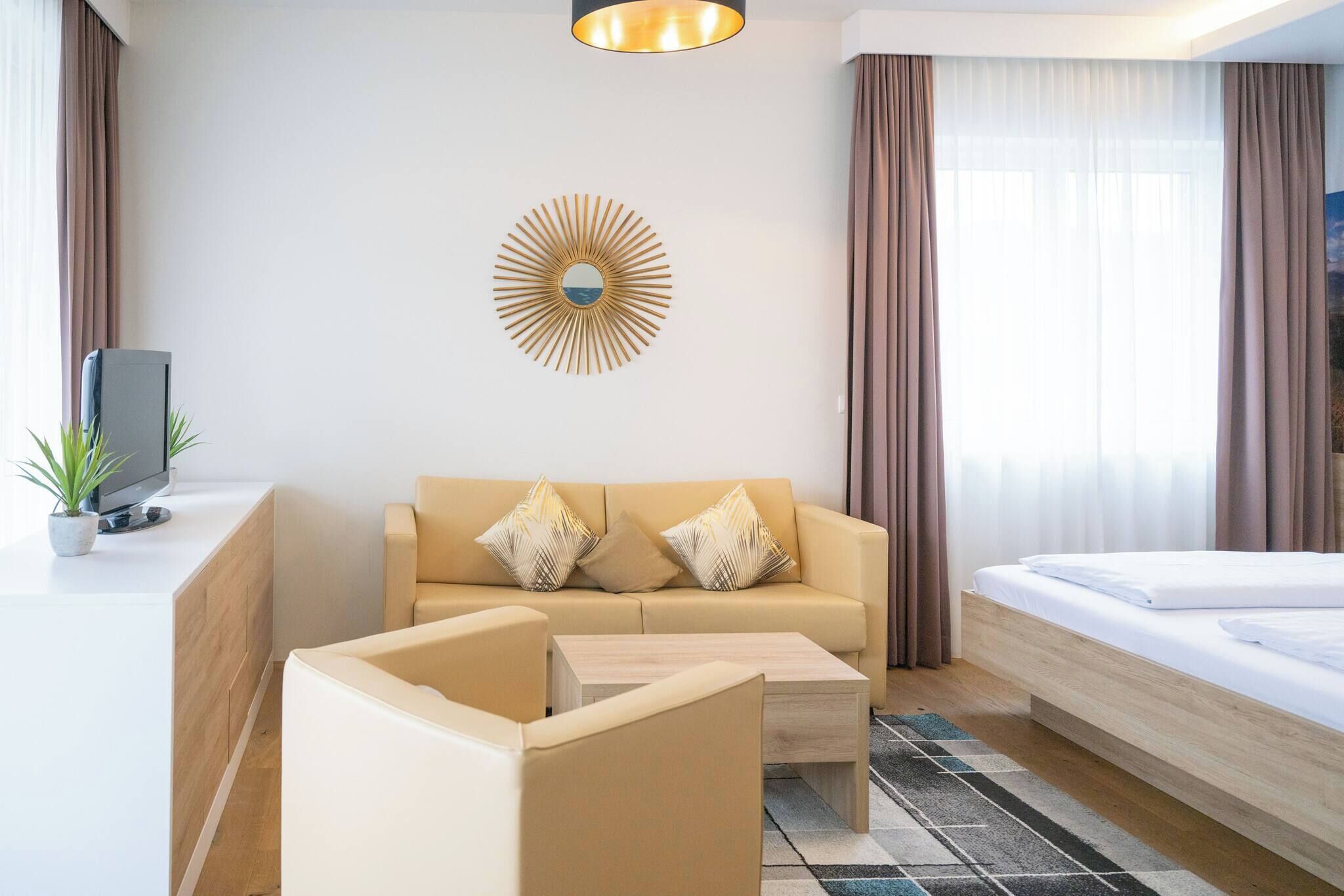 A hotel room with a sofa, a bed, a TV, a coffee table, and a decorative mirror.