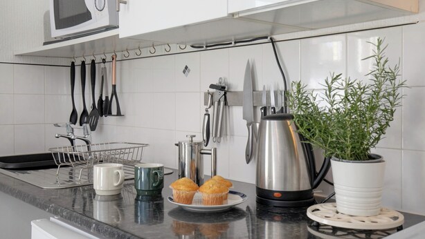 Eine K üche mit Mikrowelle, Geschirr, einer Kaffeemaschine, einem Blumentopf und Muffins auf der Arbeitsfläche.