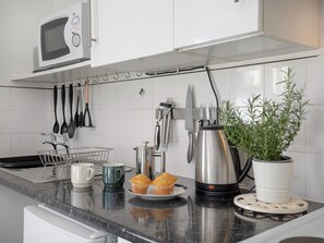 A kitchen with a microwave, utensils, a coffee maker, a potted plant, and muffins on the counter. - 1 bedroom accommodation in Paignton (Paignton)
