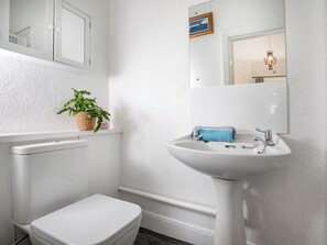 Ein Badezimmer mit Toilette, Waschbecken, einem Spiegel und einer Topfpflanze.