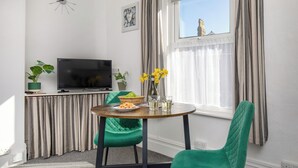 Ein modernes Wohnzimmer mit Fernseher, grünen Sesseln, einem Esstisch mit Speisen und einem Fenster mit Vorhängen.