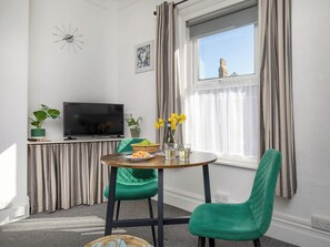 Ein modernes Wohnzimmer mit Fernseher, grünen Sesseln, einem Esstisch mit Speisen und einem Fenster mit Vorhängen.