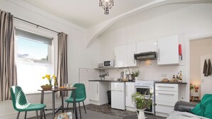 Eine kompakte Küche mit weißen Schränken, einer Mikrowelle, einem Herd und einem Spülbecken. Es gibt einen Essbereich mit Tisch und Stühlen sowie eine Wohnbereich mit einer Couch.