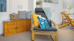 Quarto com um armário de madeira, uma poltrona cinza com almofadas, uma mesa de vidro com um vaso e um quadro na parede.