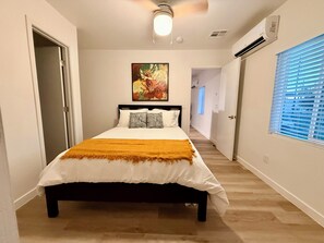 A bedroom with a bed, a painting, and a hallway leading to another room.