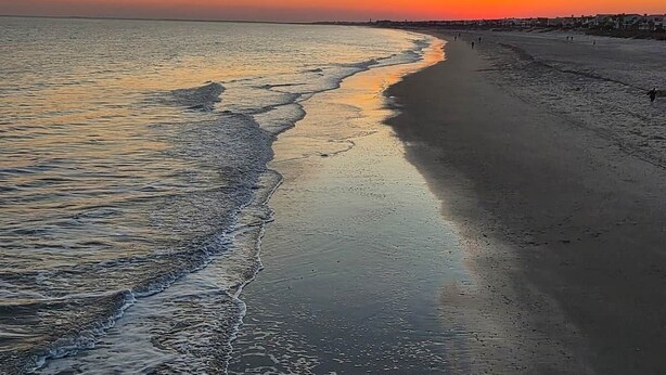 Una spiaggia al tramonto, con acqua calma e un'ampia distesa di sabbia.