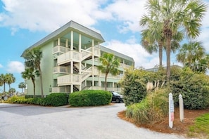 A two-story building with a balcony on the second floor, surrounded by greenery and palm trees. - Oceanfront • Private Beach + Pier • Best View (Isle of Palms)
