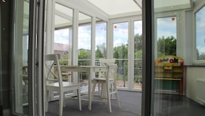 Een kamer met een glazen deur naar een balkon, een witte tafel met stoelen, en een kinderspeelruimte met kleurrijk meubilair.
