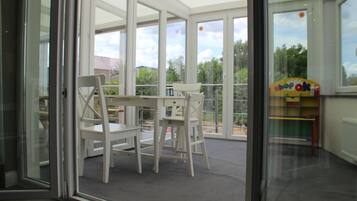 A room with a glass door leading to a balcony, a white table with chairs, and a children's play area with colorful furniture.