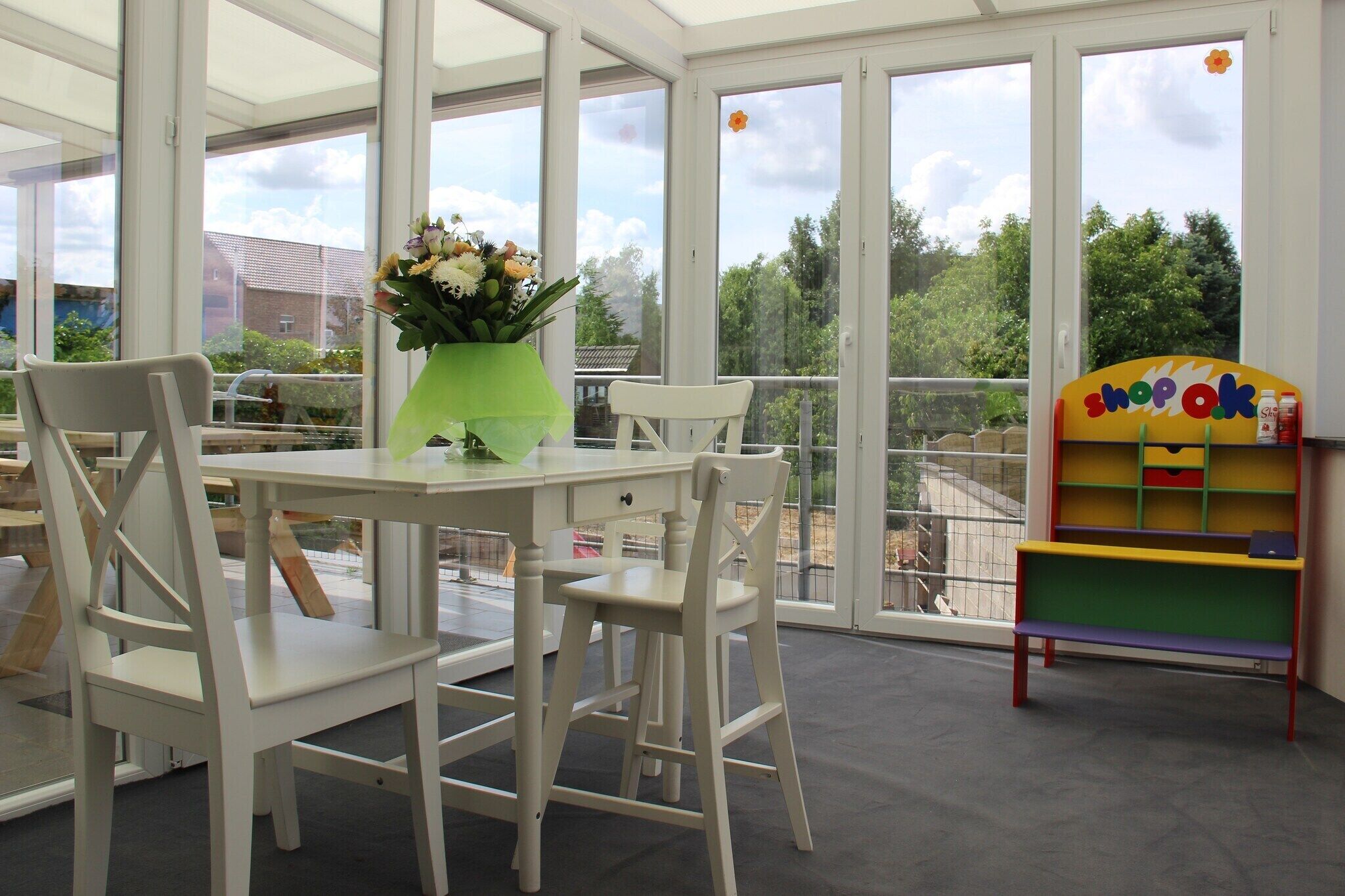 A room with a table and chairs, a vase with flowers, and a colorful bookshelf.