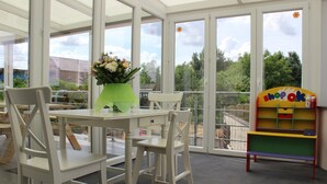 Een kamer met een tafel en stoelen, een vaas met bloemen en een kleurrijke boekenkast.
