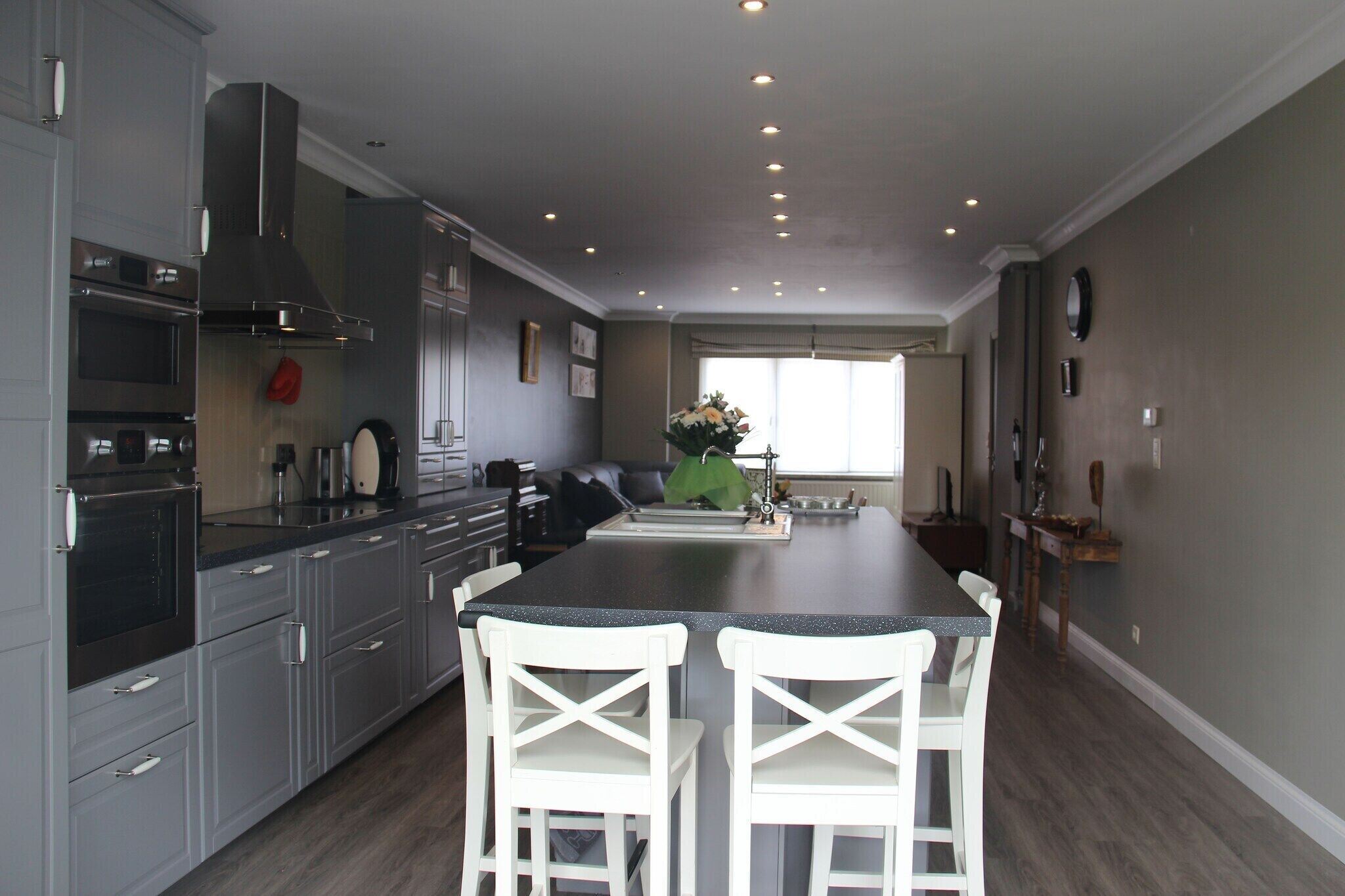 A modern kitchen with grey cabinets, a black countertop, and two white chairs.