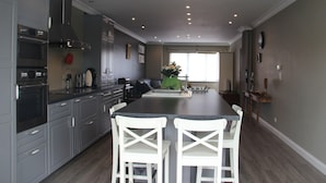 Een moderne keuken met grijze kastjes, een zwart aanrecht en twee witte stoelen.