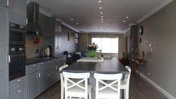A modern kitchen with grey cabinets, a black countertop, and two white chairs.