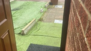 Vista d'un carrer residencial amb una furgoneta vermella aparcada, un jardí amb gespa i una casa de maó amb teules.