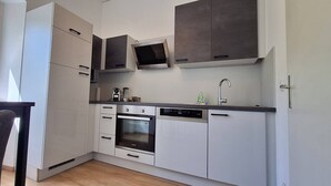A modern kitchen with white cabinets, a built-in oven, a dishwasher, and a window providing natural light.