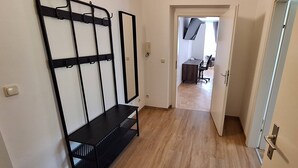 A hallway with a black metal rack, a wooden floor, and a door leading to a room with a desk and chair.