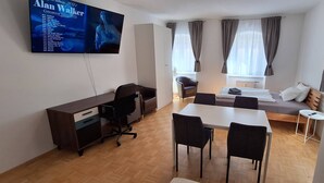 A compact hotel room with a bed, a desk, a chair, a TV, and a window with curtains.