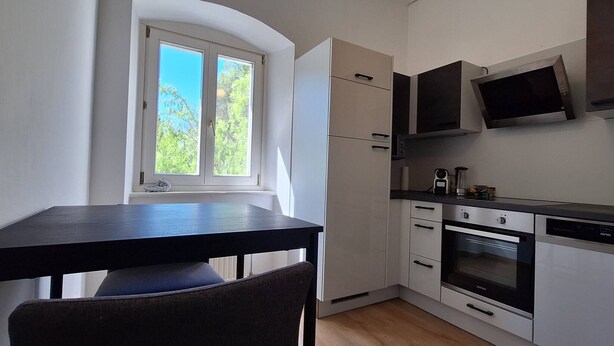 A compact kitchen with white cabinets, a black countertop, and a window with a view of trees.