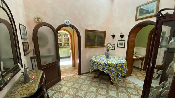 Ein Zimmer mit einem gemusterten Boden, einem runden Tisch mit einer blumigen Tischdecke und einer Tür zu einem weiteren Raum.