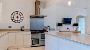 Una cocina moderna con una isla central, horno empotrado, campana extractora de acero inoxidable y un reloj de pared.