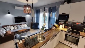 A modern kitchen with a built-in oven, a dining area with a table and chairs, a sofa, and a TV mounted on the wall. - Villa Mediterranea Seaview Primošten (Primosten)