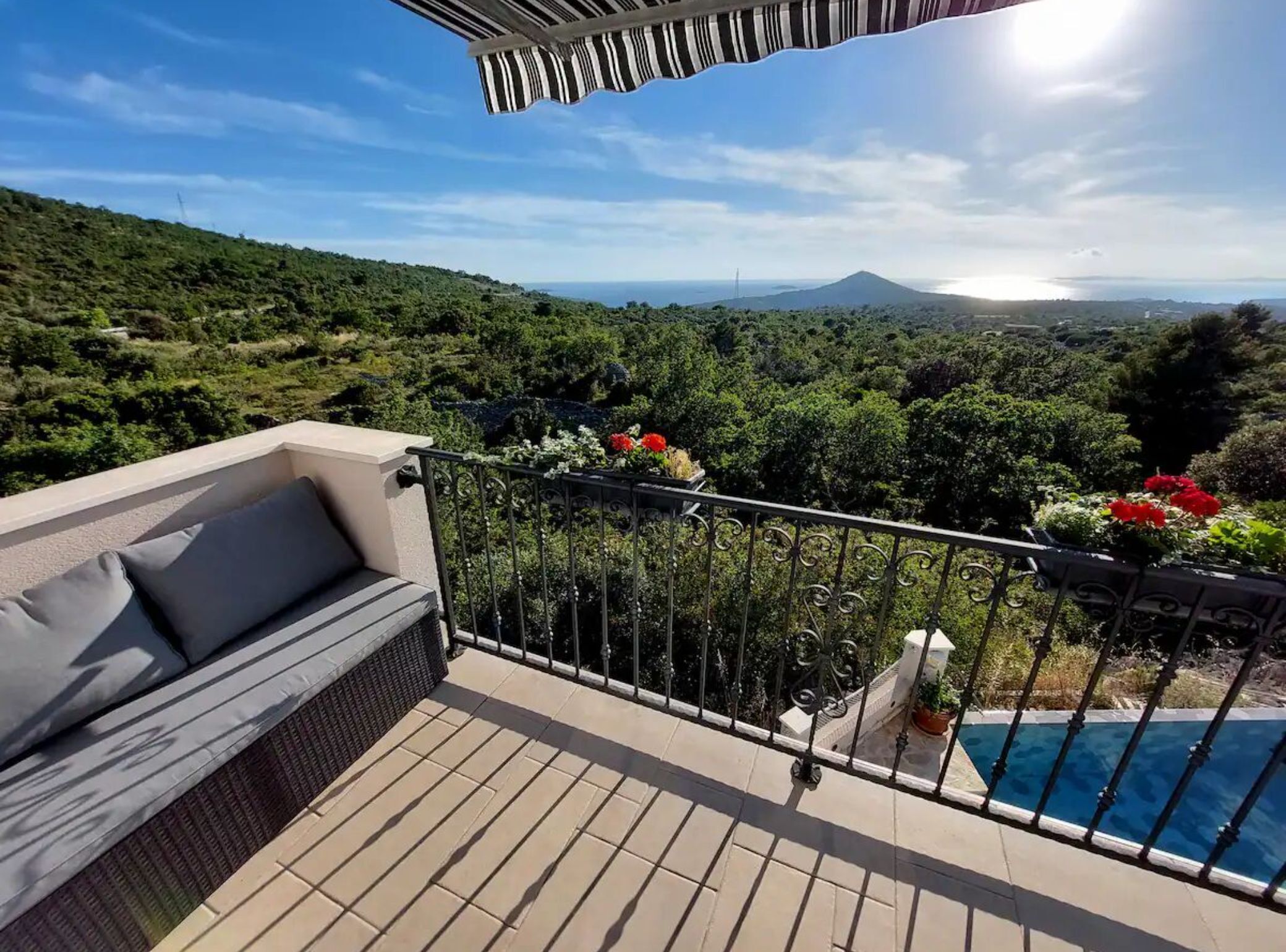 A balcony with a sofa, a pool, and a view of a mountainous landscape.
