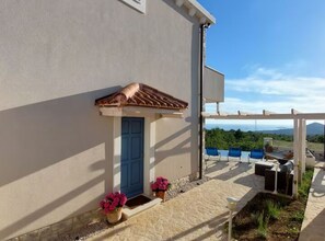 A building with a blue door, a small porch with potted plants, and a view of the landscape. - Villa Mediterranea Seaview Primošten (Primosten)