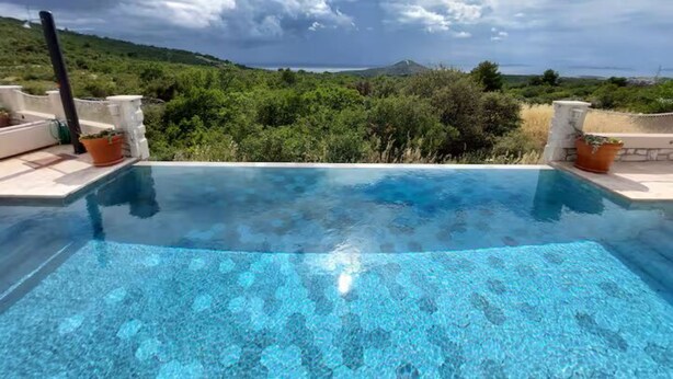 A clear blue infinity pool with a view of a mountainous landscape and greenery. - Villa Mediterranea Seaview Primošten (Primosten)