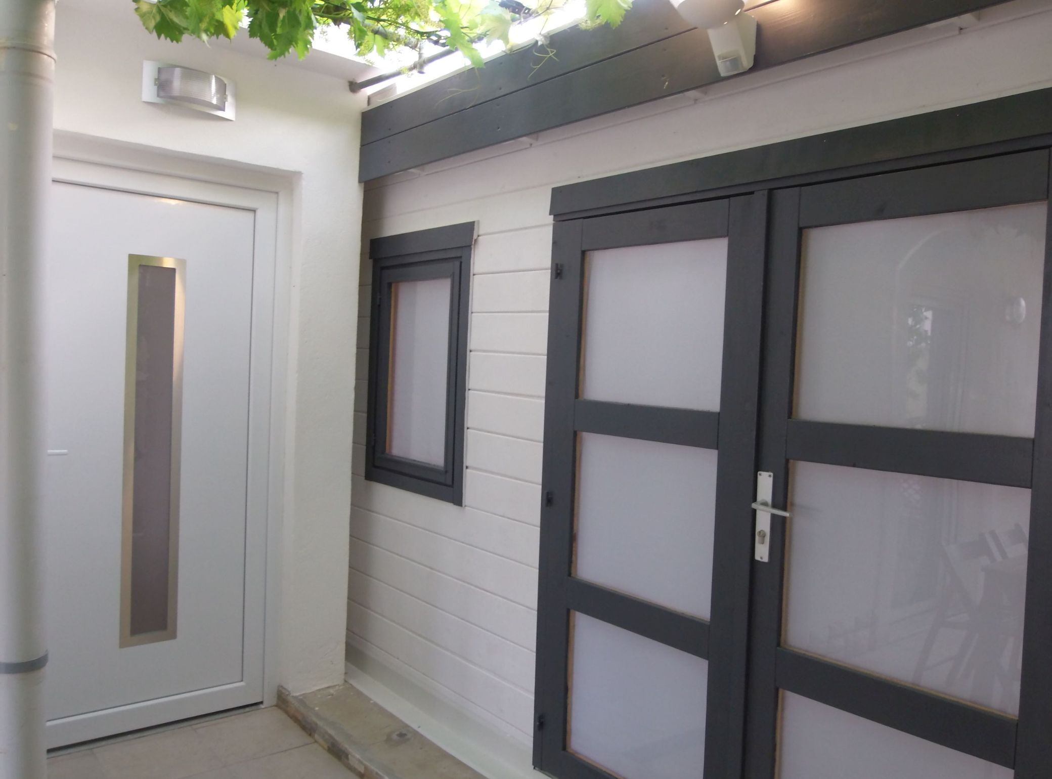 A white door with a vertical handle, a window with a black frame, and a garage door with a black frame and frosted glass panels.