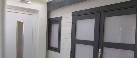 Une porte blanche avec une poignée verticale, une fenêtre avec un cadre noir et une porte de garage avec un cadre noir et des panneaux en verre dépoli.