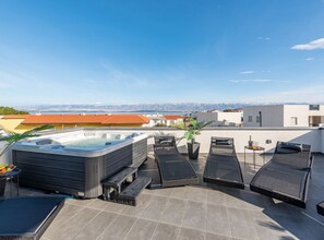 Une terrasse sur le toit équipée d’un jacuzzi, de chaises longues et offrant une vue sur le paysage urbain.