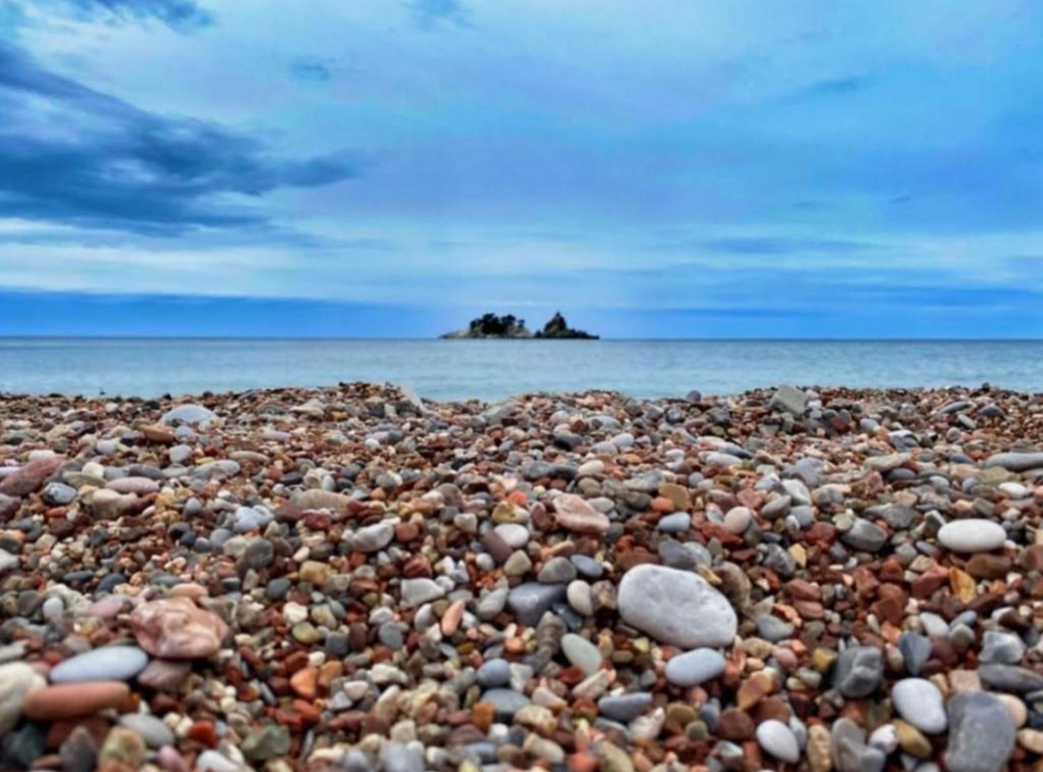A pebbled beach with a distant rocky outcrop.