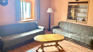 Una sala de estar con dos sofás, una mesa, una lámpara, una ventana y una estantería en la pared.