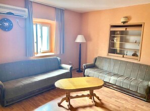 A living room with two sofas, a table, a lamp, a window, and a wall-mounted shelf. - Villa Teodora Mare (Petrovac)