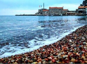 A coastal scene with a pebbled beach, a building with a red roof, and a body of water. - Villa Teodora Mare (Petrovac)