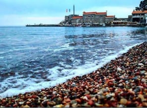 Eine Küstenlandschaft mit Kiesstrand, einem Gebäude mit rotem Dach und einer Wasserfläche.