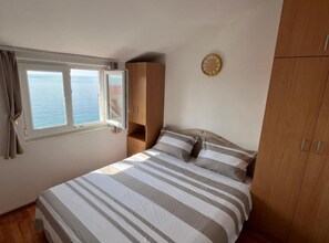 A bedroom with a bed, a wooden wardrobe, a window with curtains, and a wall clock. - Villa Teodora Mare (Petrovac)