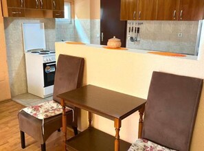 A compact kitchen with a stove, refrigerator, and a small table with two chairs. - Villa Teodora Mare (Petrovac)